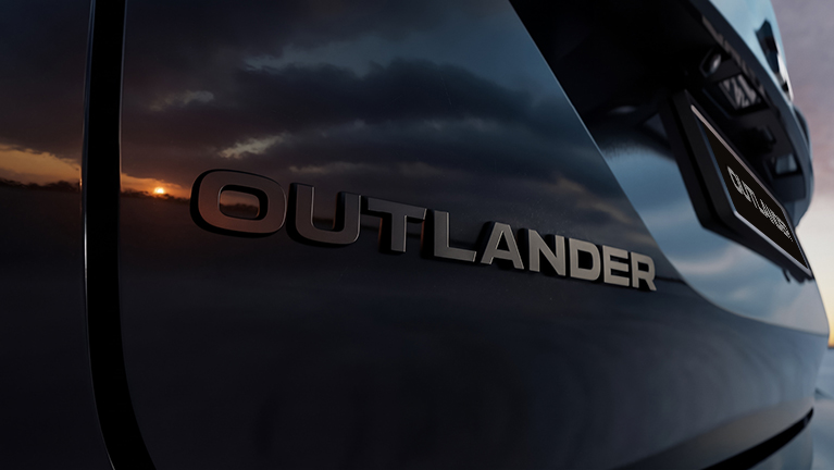 Nahaufnahme des Outlander-Schriftzugs auf der dunklen Karosserie des Mitsubishi Outlander Black